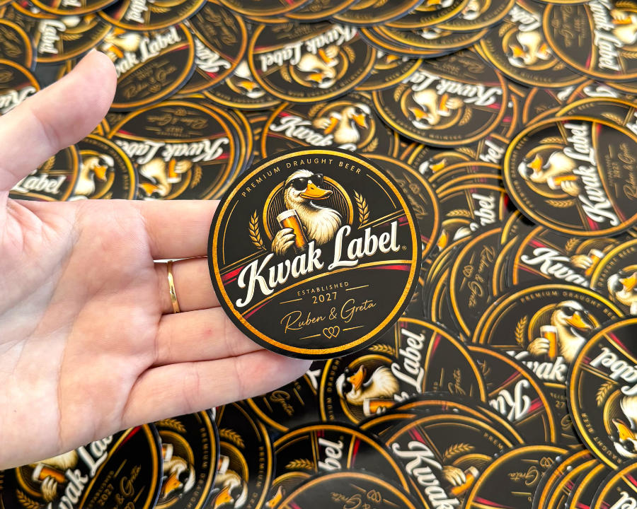 Round black and gold Kwak Label beer stickers, one held in an open hand