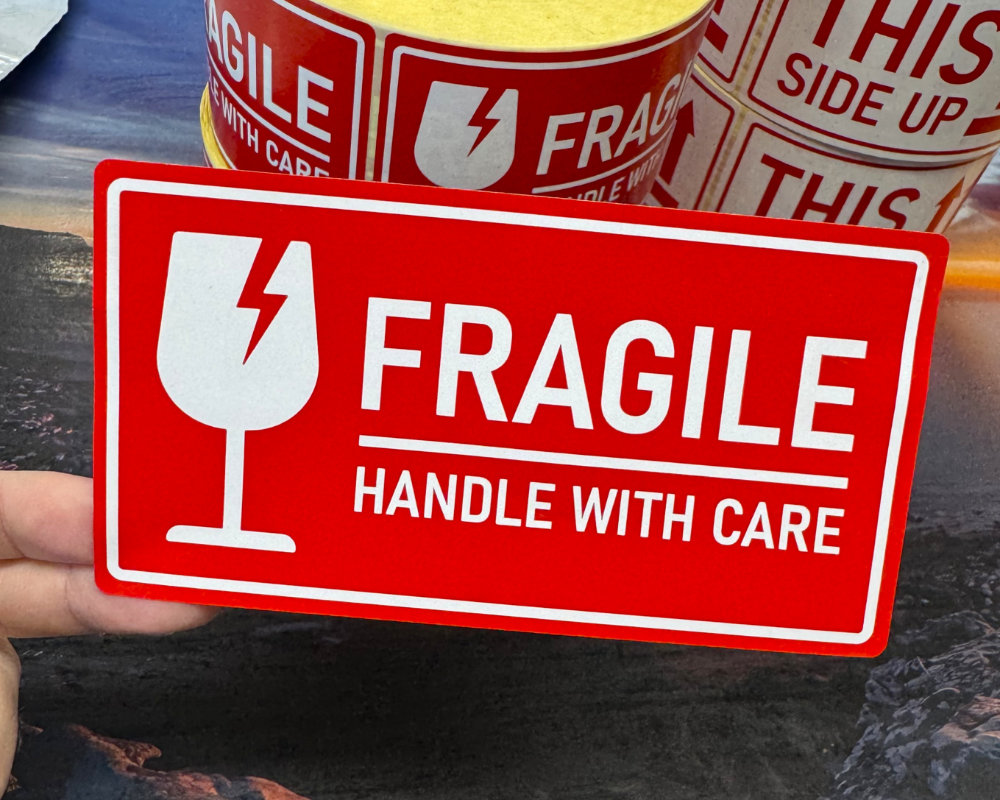 Red and white Fragile Handle With Care warning labels held up in front of stacked rolls